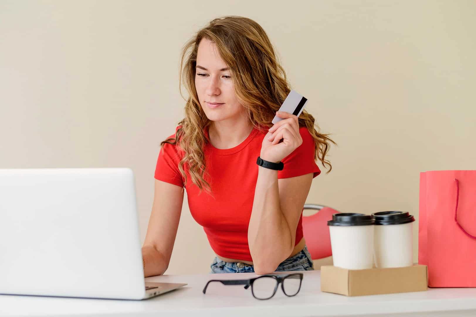 Kobieta trzymająca kartę płatniczą podczas zakupów online przy laptopie – decyzja o odstąpieniu od umowy.