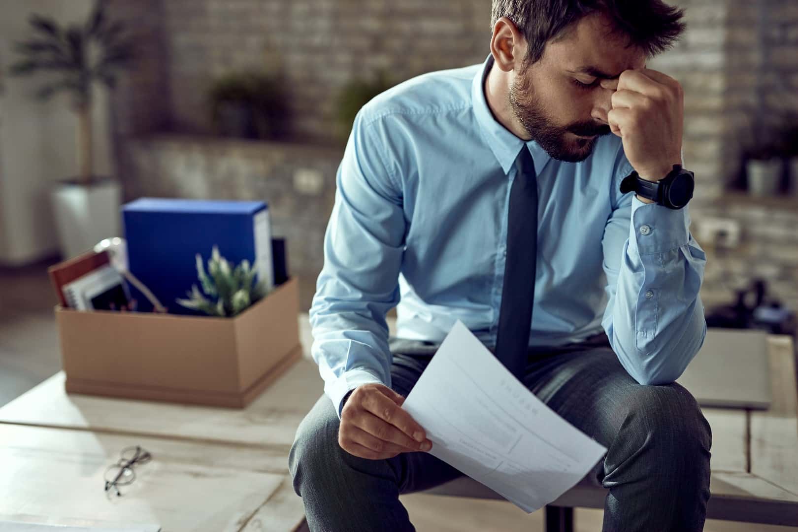 Zmartwiony mężczyzna w koszuli i krawacie siedzący z dokumentem w ręku – symbol problemów finansowych i zadłużenia.